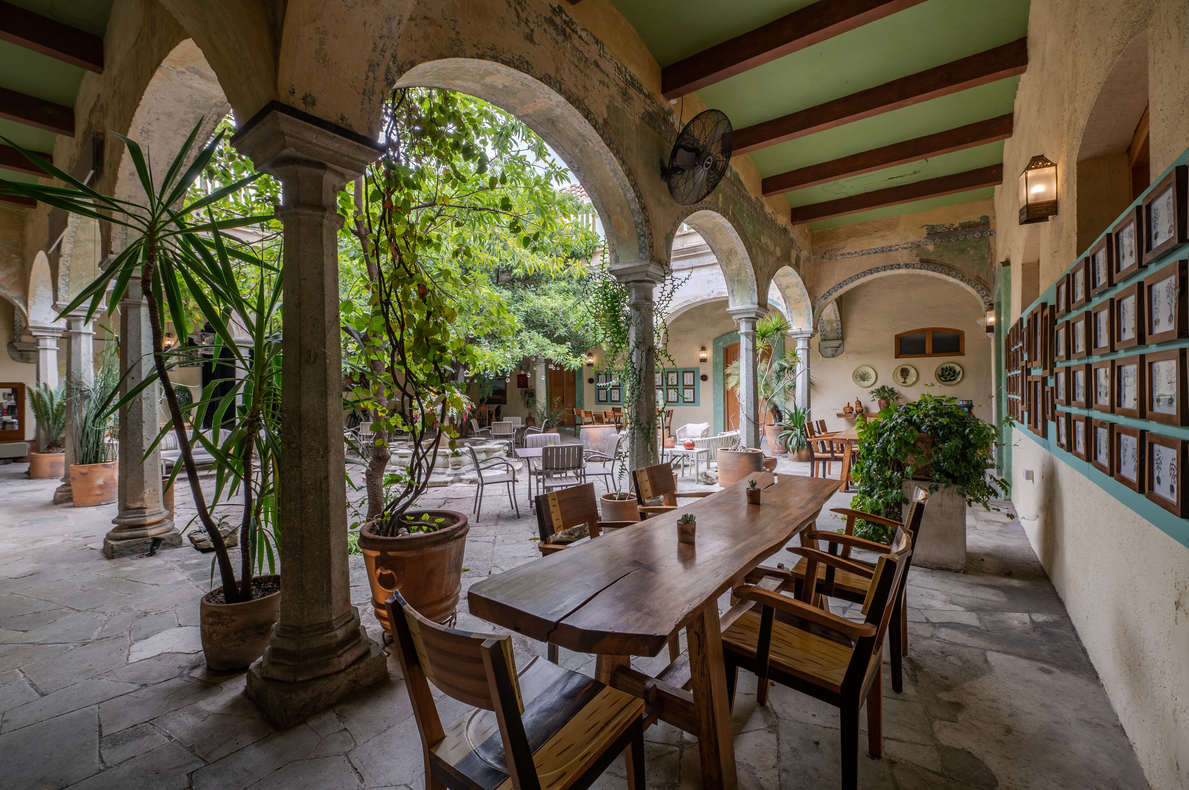 A spacious courtyard with a wooden table and chairs, surrounded by arches and potted plants.