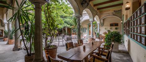 A spacious courtyard with a wooden table and chairs, surrounded by arches and potted plants.