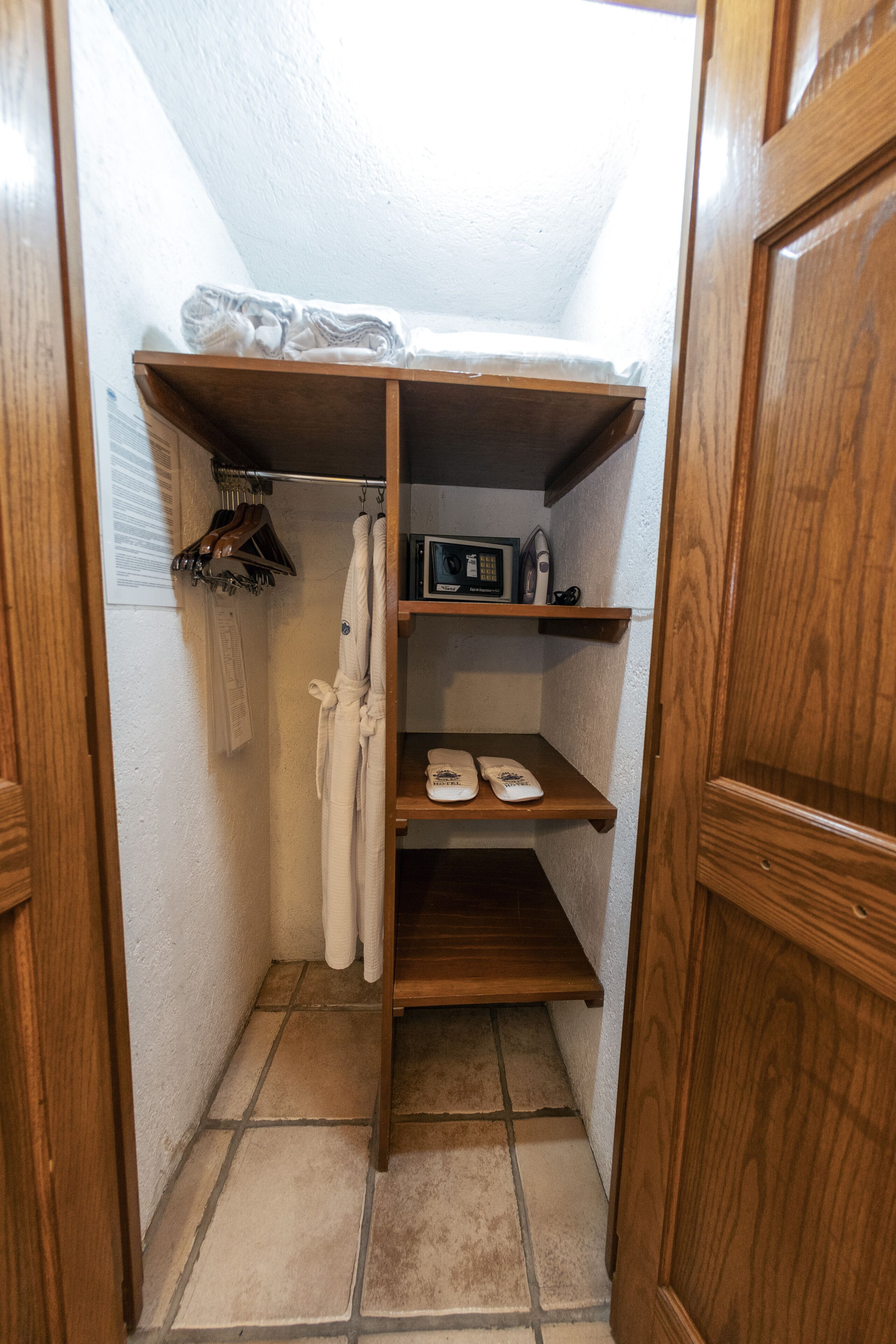 A small, compact bathroom with a shower, a wooden shelf with toiletries, and a towel rack.