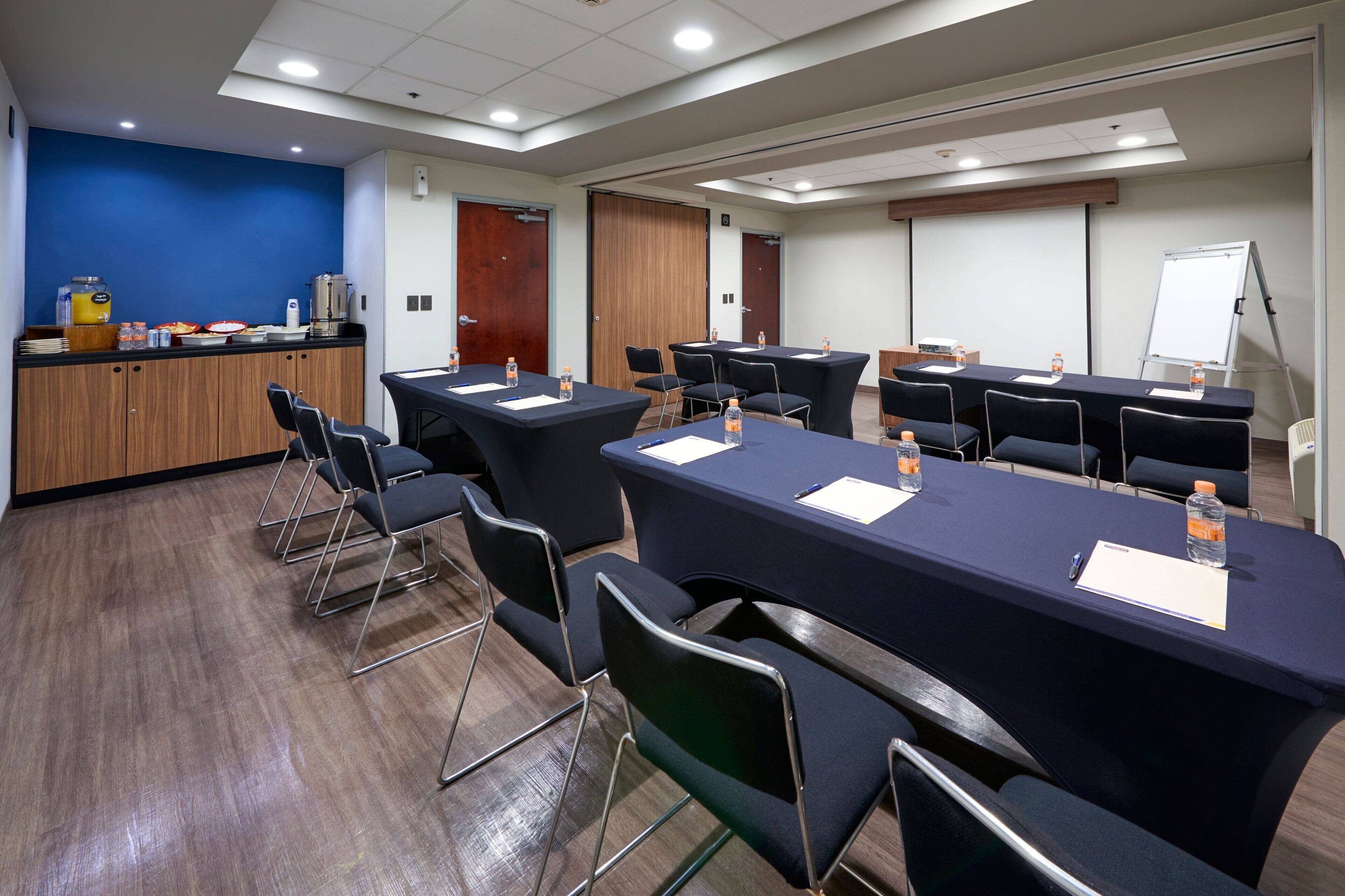 A conference room with multiple tables and chairs, a coffee station, and a whiteboard.