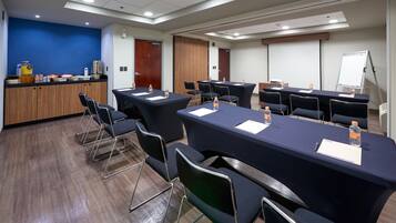 A conference room with multiple tables and chairs, a coffee station, and a whiteboard.