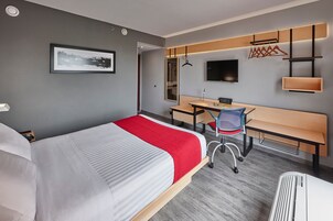 A modern hotel room with a large bed, a desk, a chair, a bench, a TV, and a wardrobe.