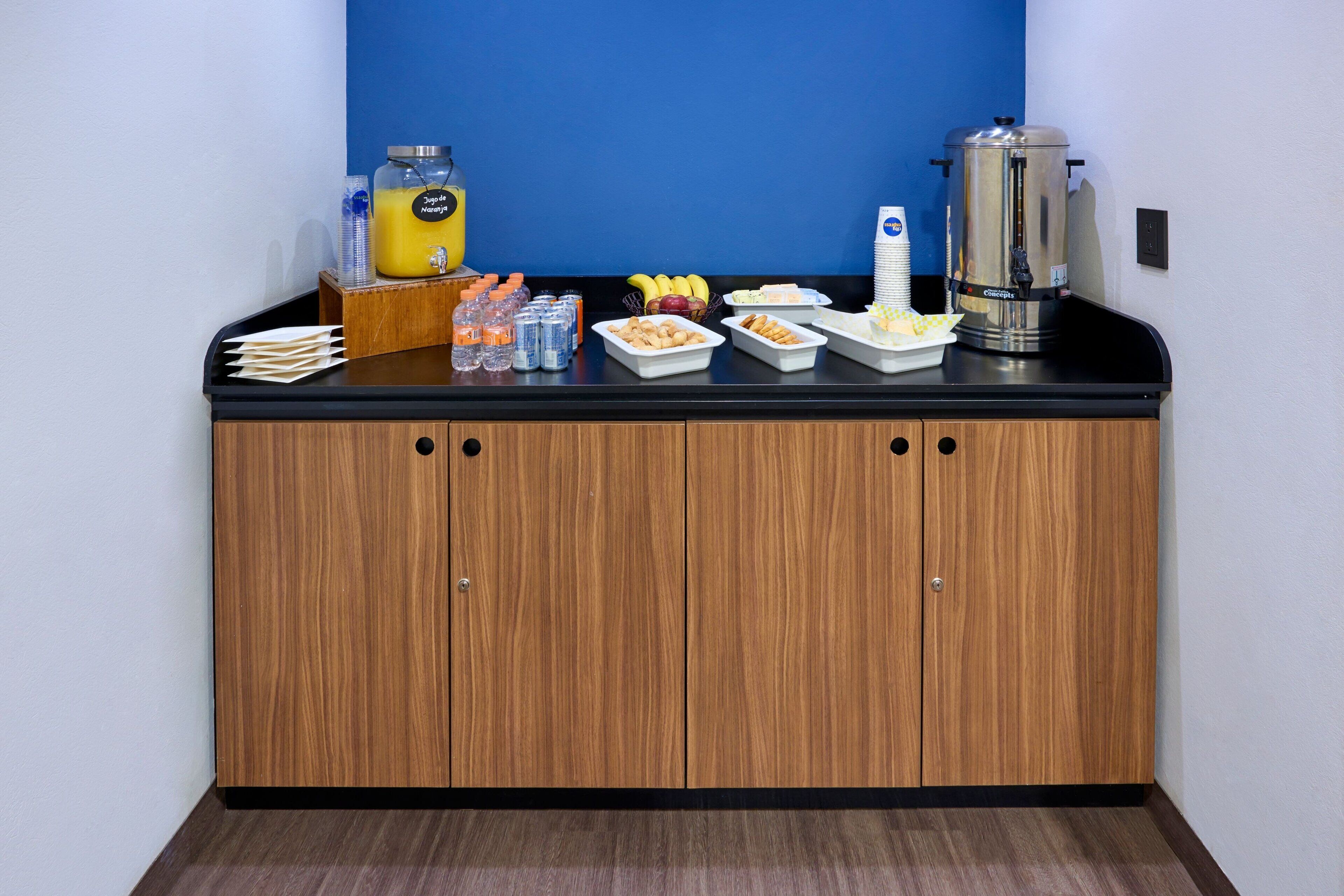 A breakfast bar with various food items, a coffee maker, and a juice dispenser.