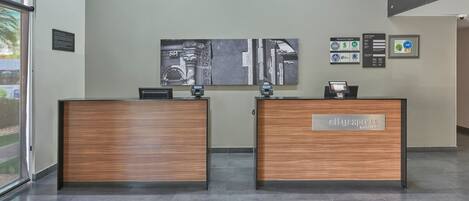 Un mostrador de recepción con acabado de madera y una pantalla digital, una gran obra de arte abstracta en la pared, y una placa con logotipos.
