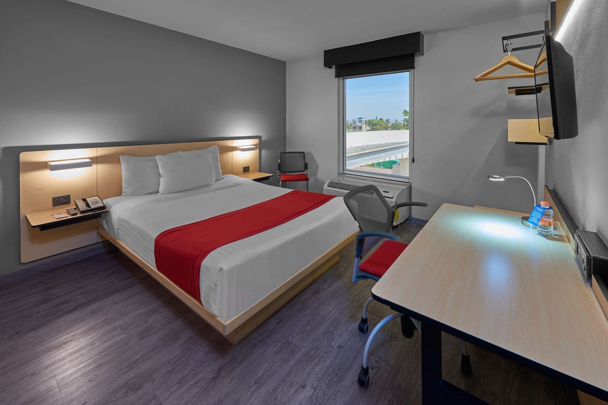 A hotel room with a bed, bedside table, desk, chair, and a window with a view.