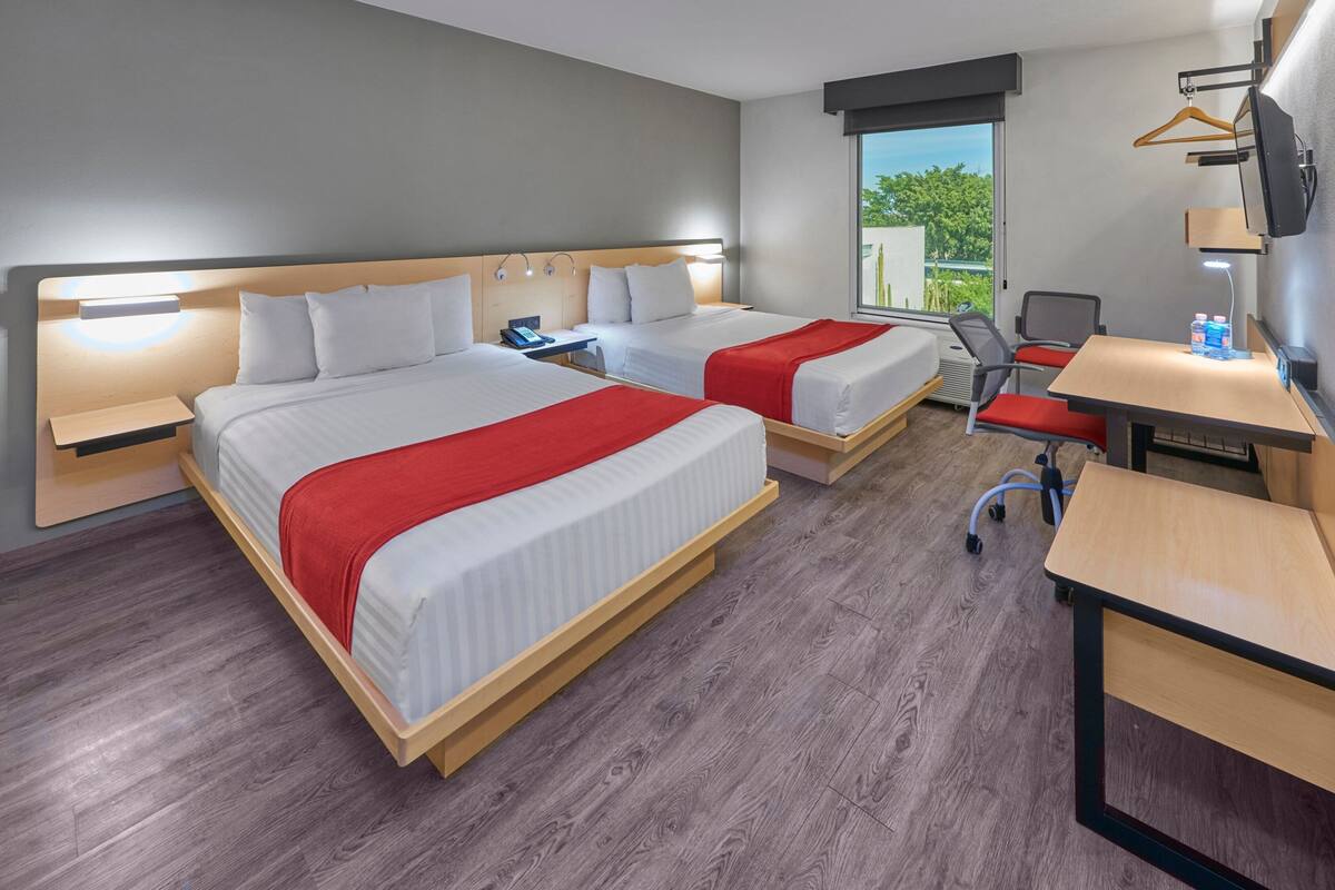 A hotel room with two beds, a desk, a chair, and a TV.