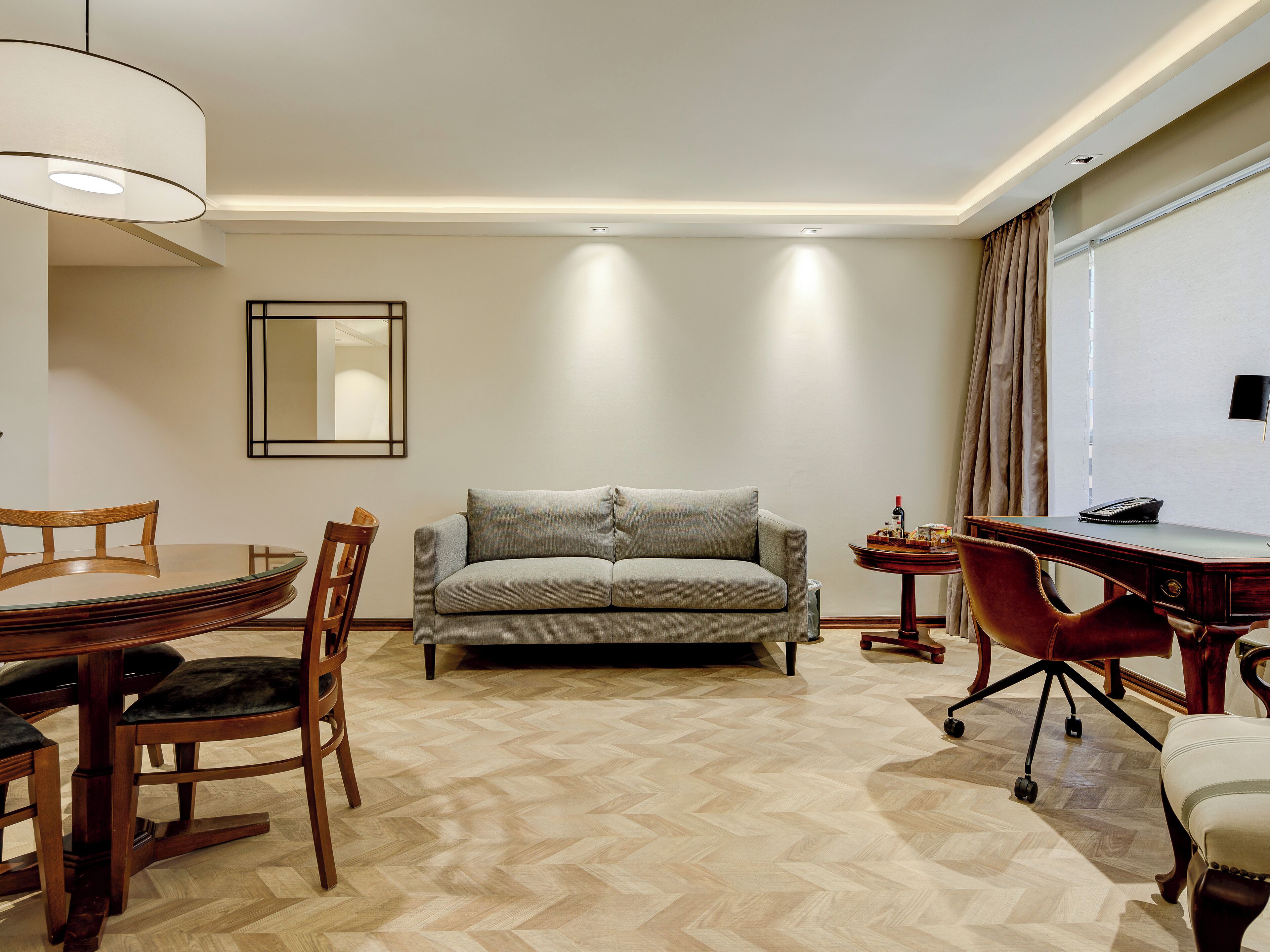 Een moderne hotelkamer met een bank, eettafel, stoelen, bureau en lamp.