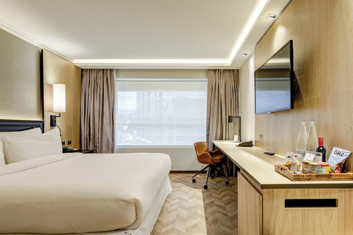 A hotel room with a large bed, a desk with a chair, a TV, and a window with curtains.