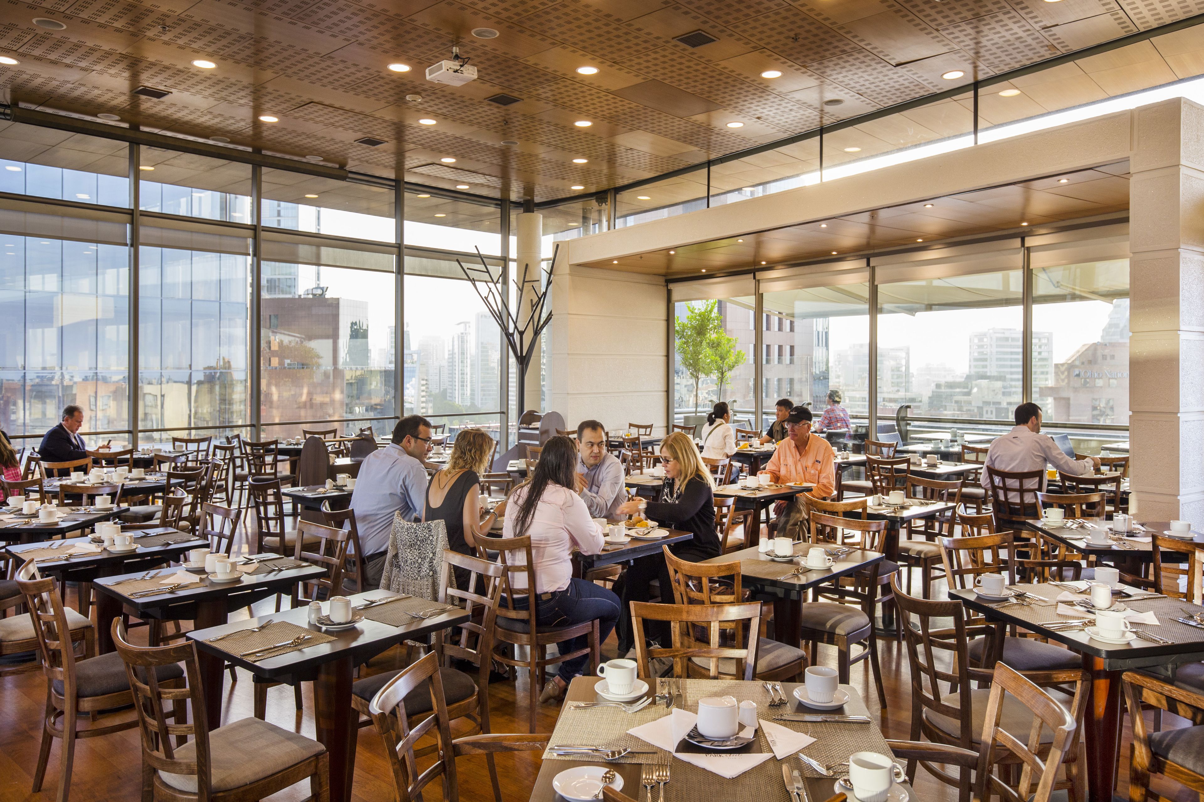A spacious dining area with multiple tables and chairs, large windows offering views of the cityscape.
