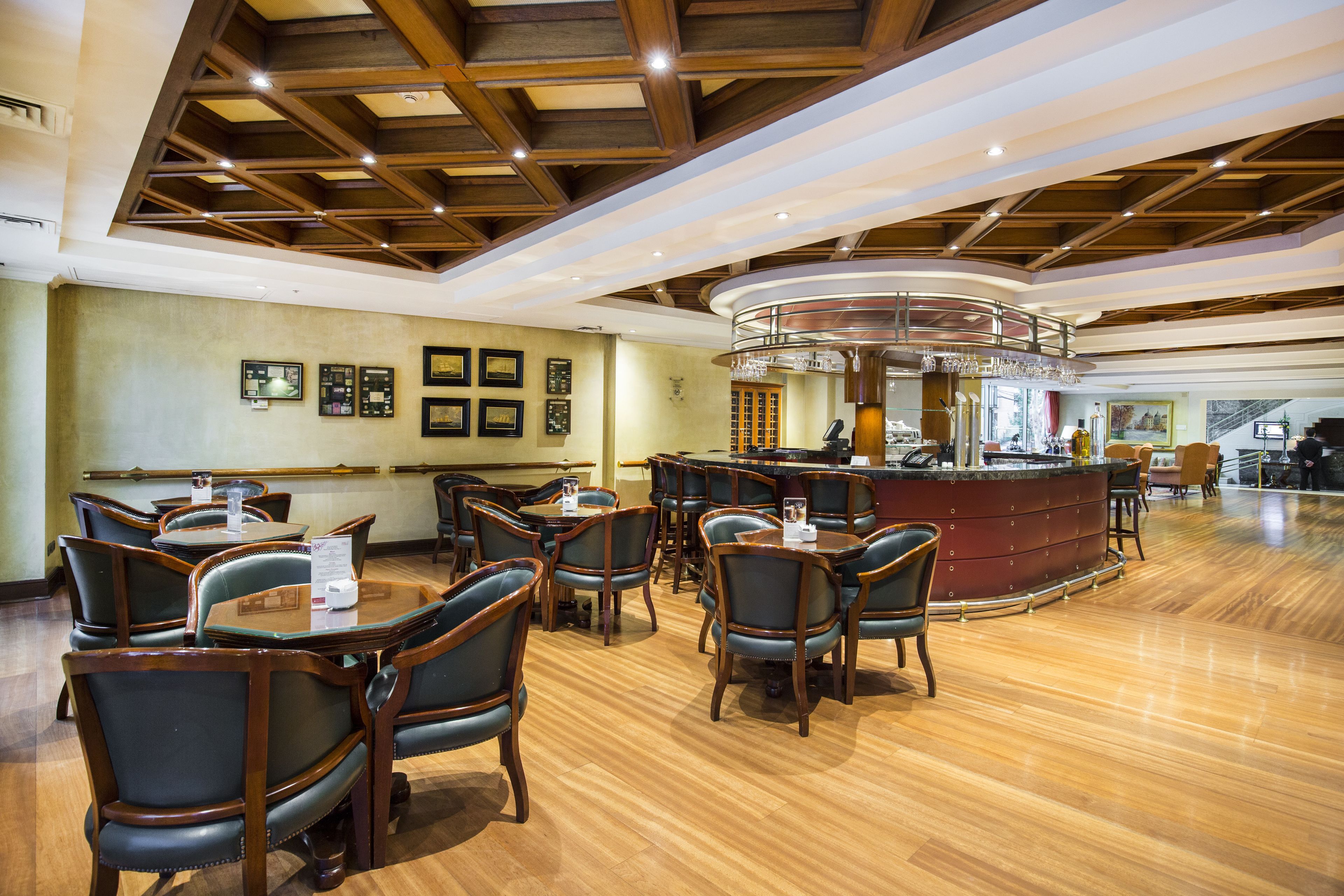 A spacious restaurant with wooden flooring, dark leather chairs, and a central bar area.