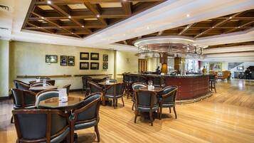 A spacious restaurant with wooden flooring, dark leather chairs, and a central bar area.