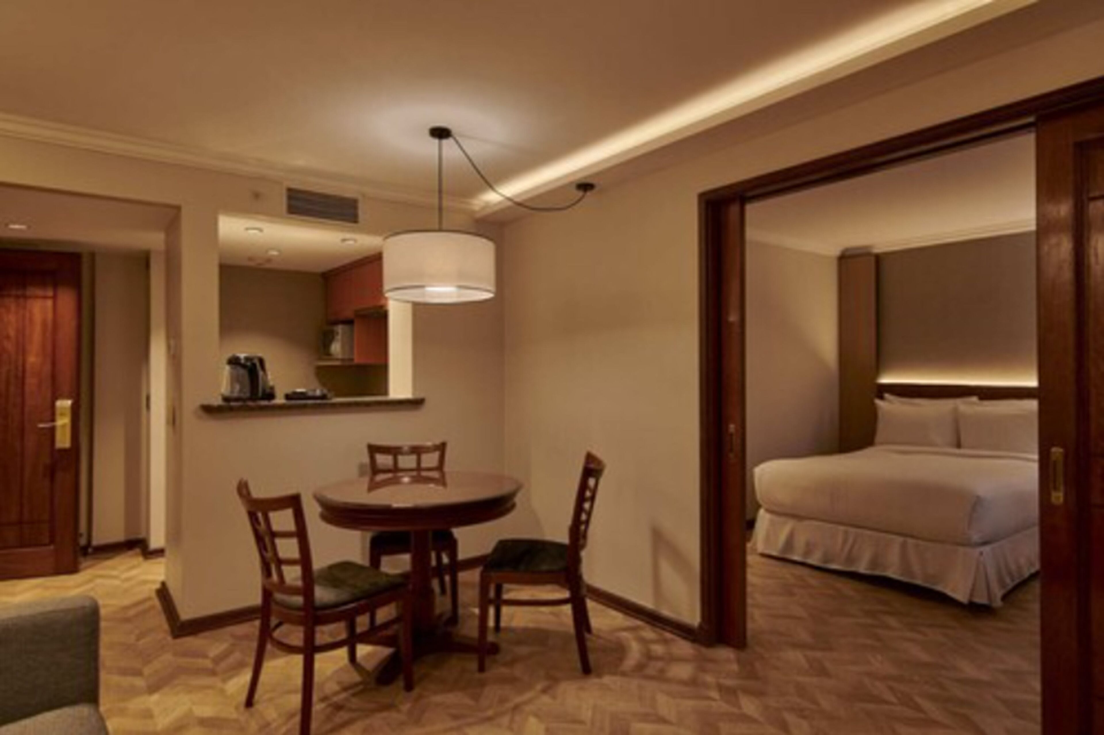 Ein Hotelzimmer mit Bett, Esstisch mit Stühlen, einer Küchenzeile und einem Flur.