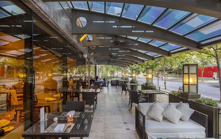 An outdoor cafe with tables and chairs, a covered seating area, and a view of the street.