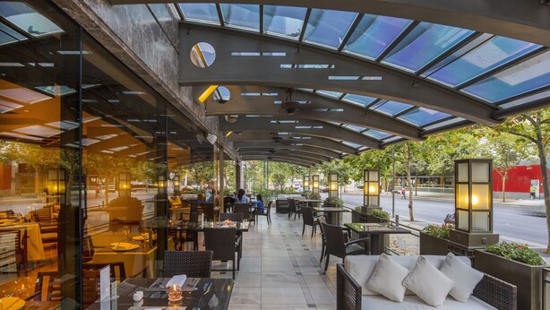 Un café al aire libre con mesas y sillas, una zona de estar cubierta y vistas a la calle.
