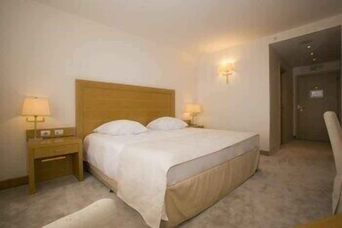 Een hotelkamer met een bed, twee nachtkastjes met lampen, een stoel en een deur.