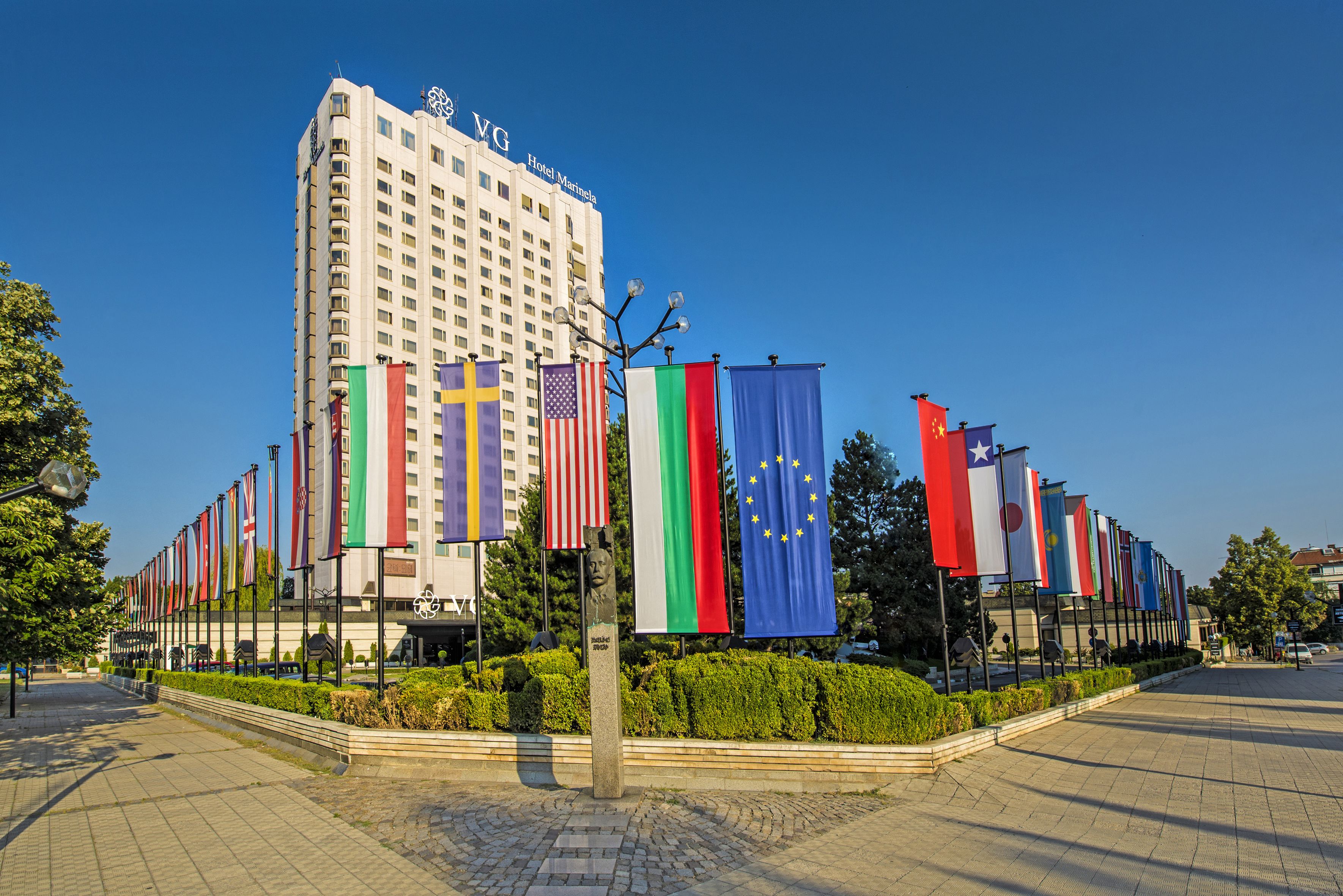 A hotel with multiple flags, a clear sky, and a paved walkway.