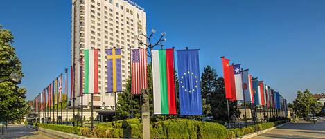 A hotel with multiple flags, a clear sky, and a paved walkway.