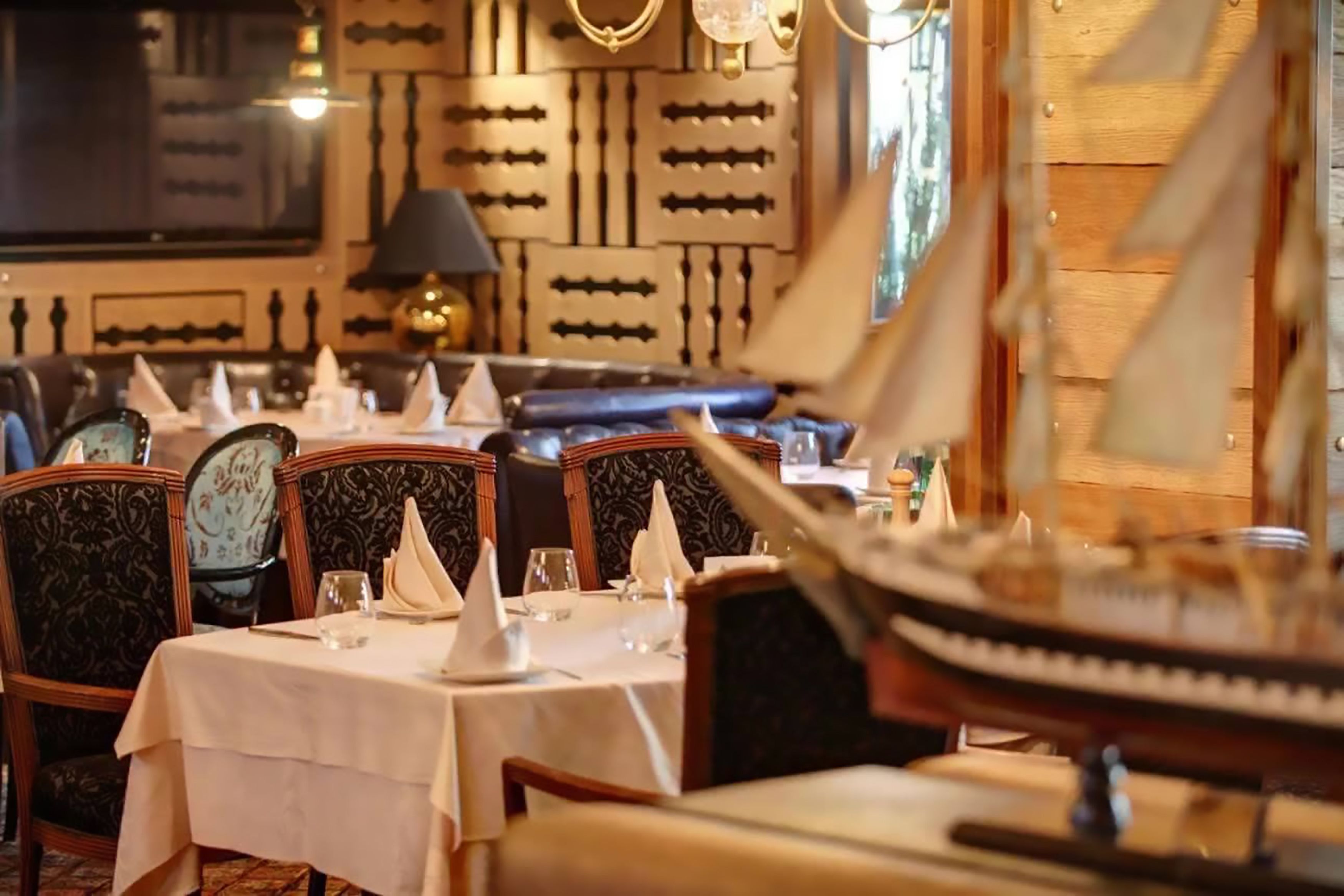 A restaurant with wooden paneling, nautical-themed decor, and a ship model on the table.