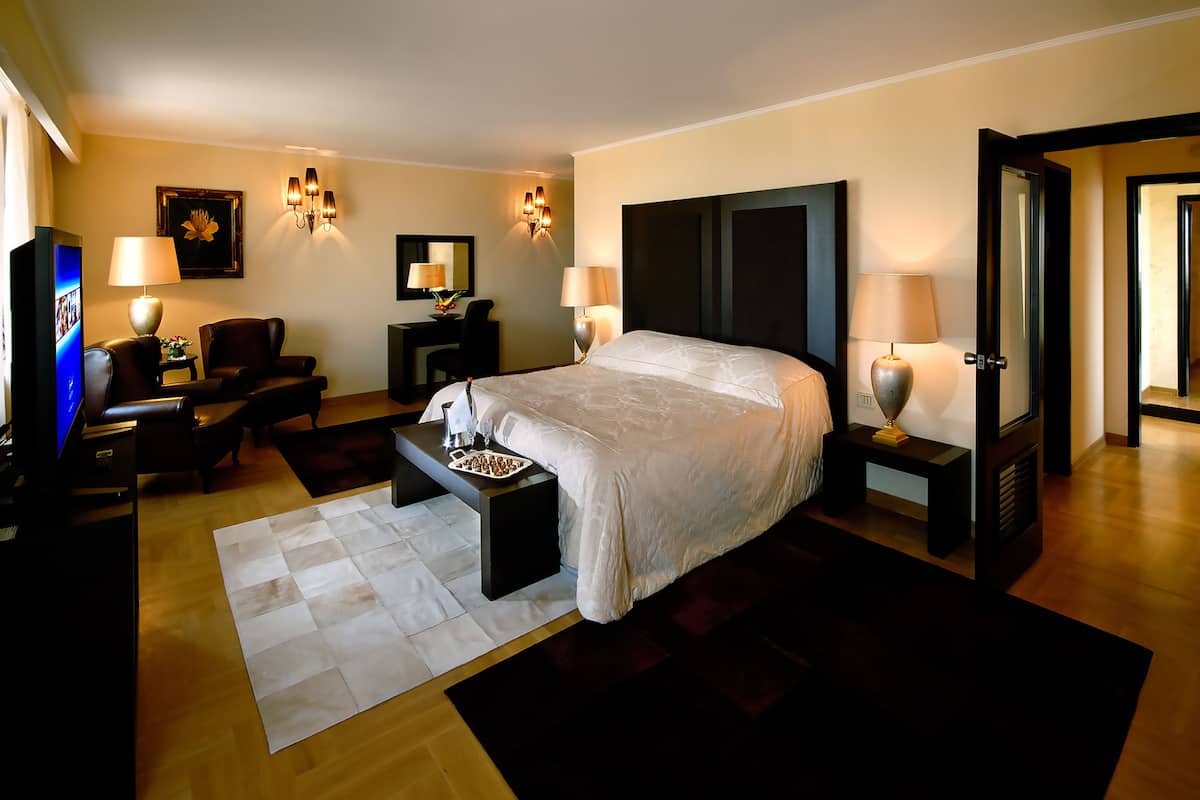 Ein Hotelzimmer mit einem großen Bett, einem Schreibtisch mit Stuhl, einem Fernseher und Wandleuchten.
