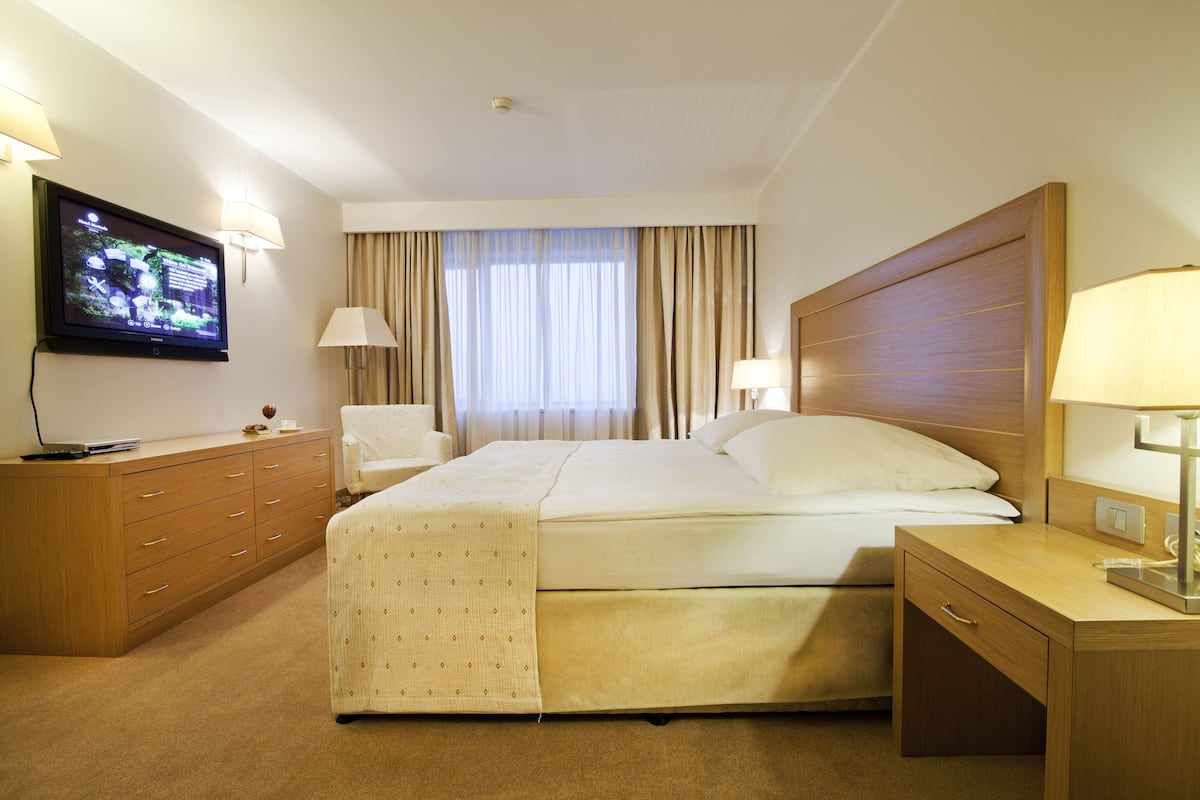 Ein Hotelzimmer mit Bett, Wandfernseher, Schreibtisch mit Lampe und Sessel.