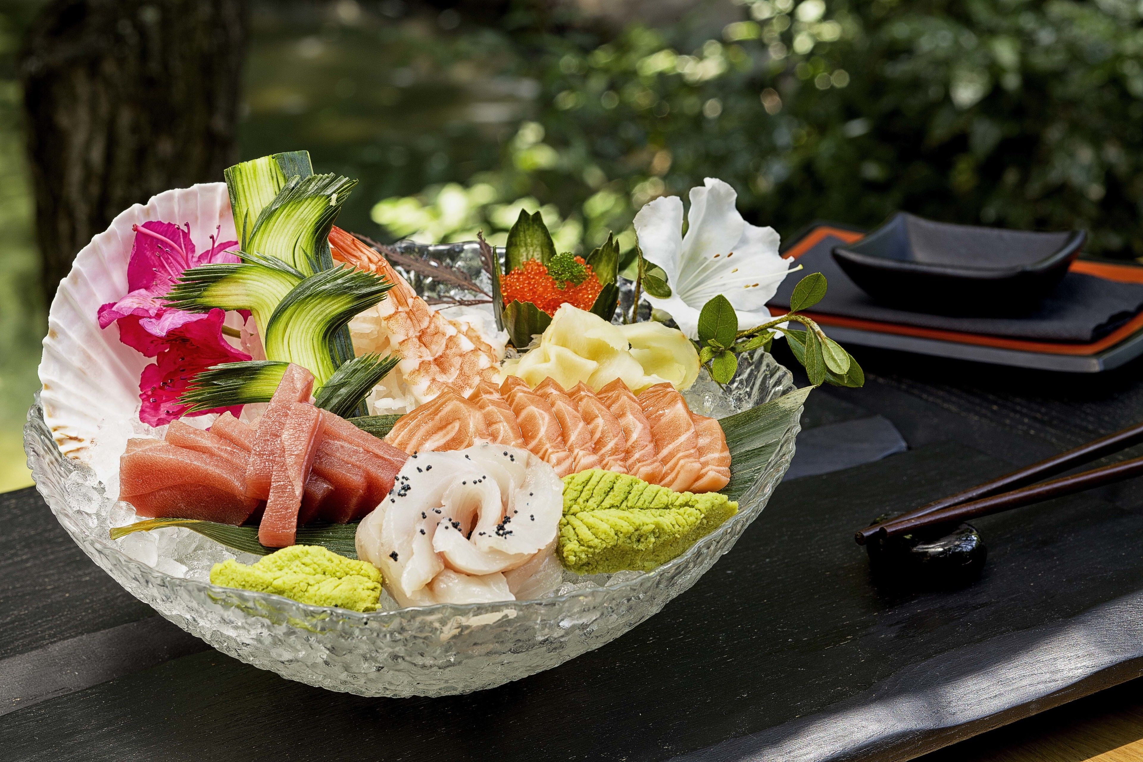 Un saladier en verre contenant divers types de sashimi et des accompagnements, le tout posé sur une table en bois.
