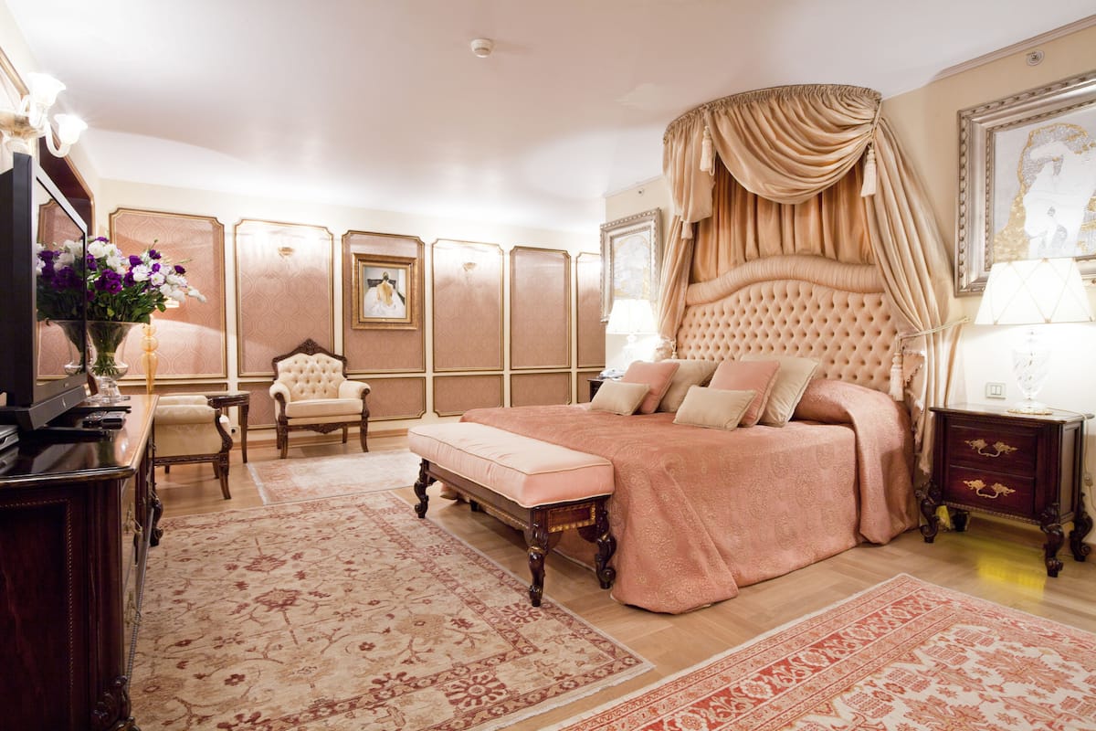 Ein Schlafzimmer mit einem großen Bett, einem Schminktisch mit Spiegel, einem Sessel und einer Kommode.