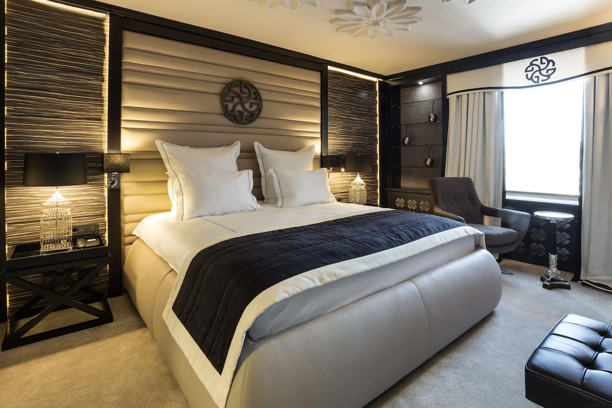 Ein modernes Schlafzimmer mit einem großen Bett, Nachttischen, einem Sessel und einem dekorativen Wandbild.