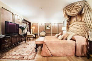 Ein luxuriöses Schlafzimmer mit einem großen Bett, einem Fernseher, einer Liege und einem dekorativen Teppich.