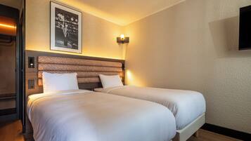 A hotel room with two beds, a headboard, a wall-mounted light fixture, and a framed picture.