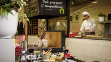 Une scène de restaurant avec une table dressée pour le dîner, un chef en train de préparer des plats et une pancarte faisant la publicité de la réservation de chambres.