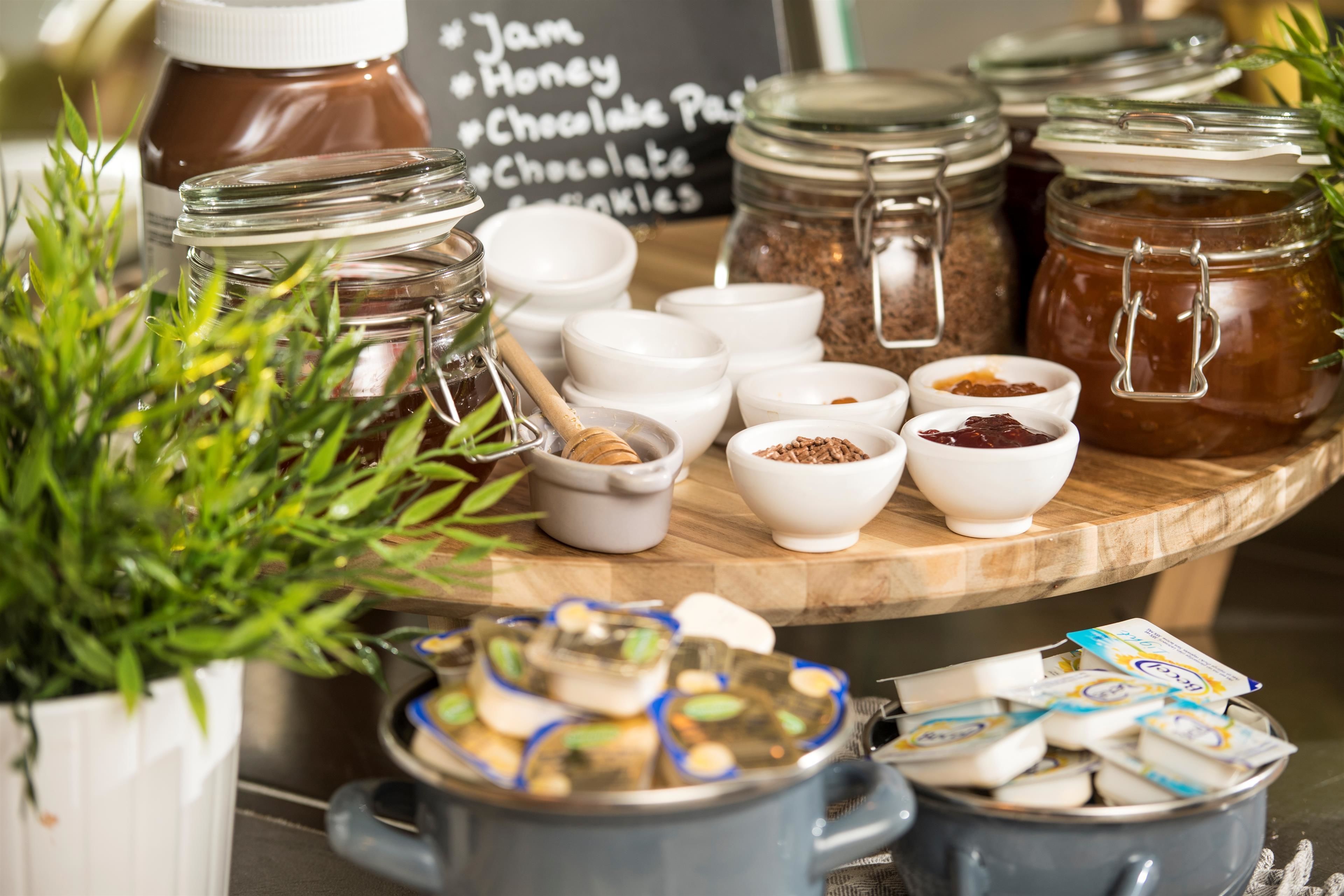 A variety of food items including jars of honey, chocolate, and jams, along with small bowls containing spices and seeds.