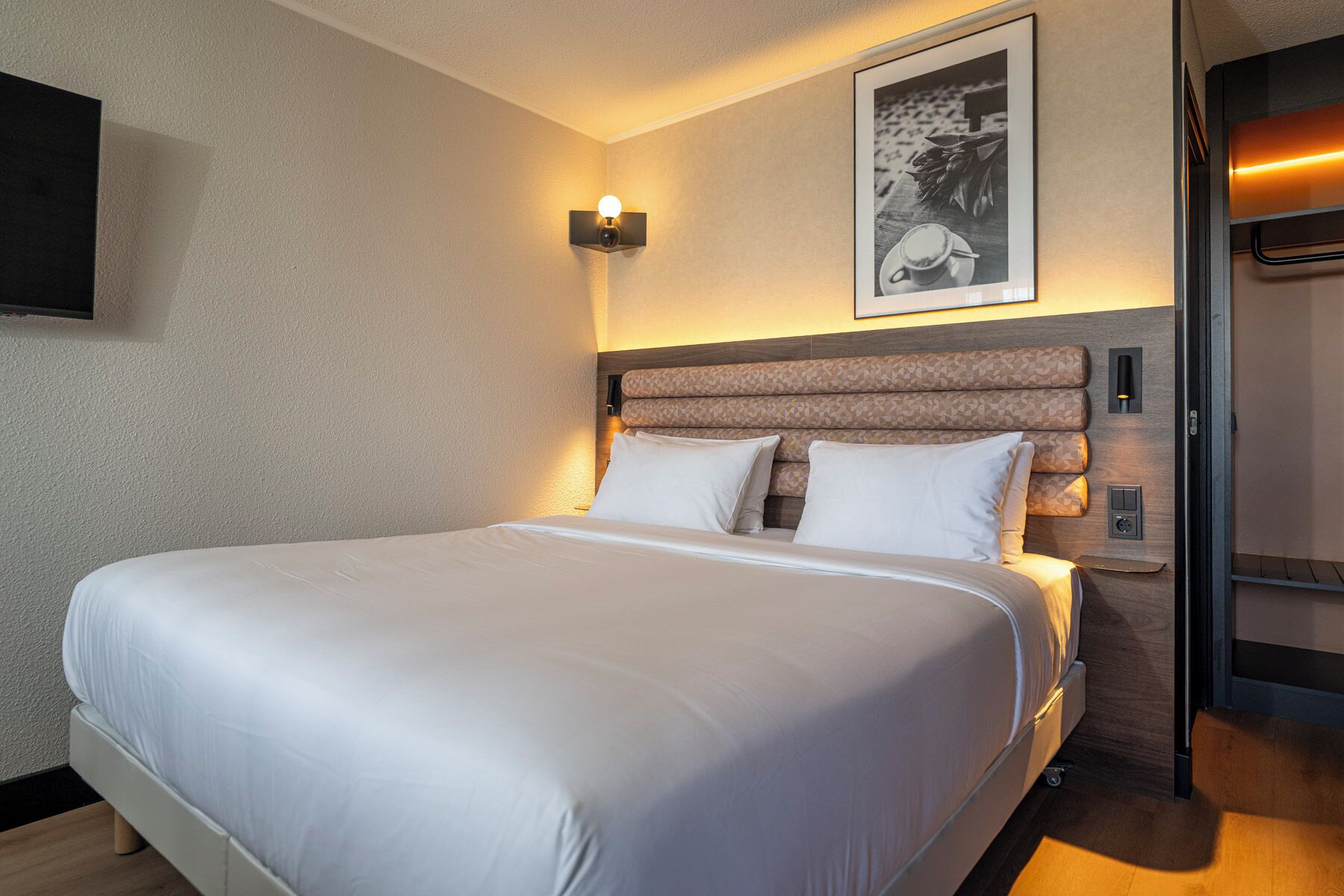 Una habitación de hotel con una cama grande, un cabecero de diseño estampado, una lámpara de pared y un cuadro enmarcado sobre la cama.