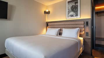 Una habitación de hotel con una cama grande, un cabecero de diseño estampado, una lámpara de pared y un cuadro enmarcado sobre la cama.