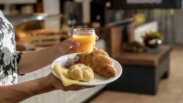 Una persona sosteniendo un plato con un croissant, un vaso de jugo de naranja y un frasco pequeño de mermelada.