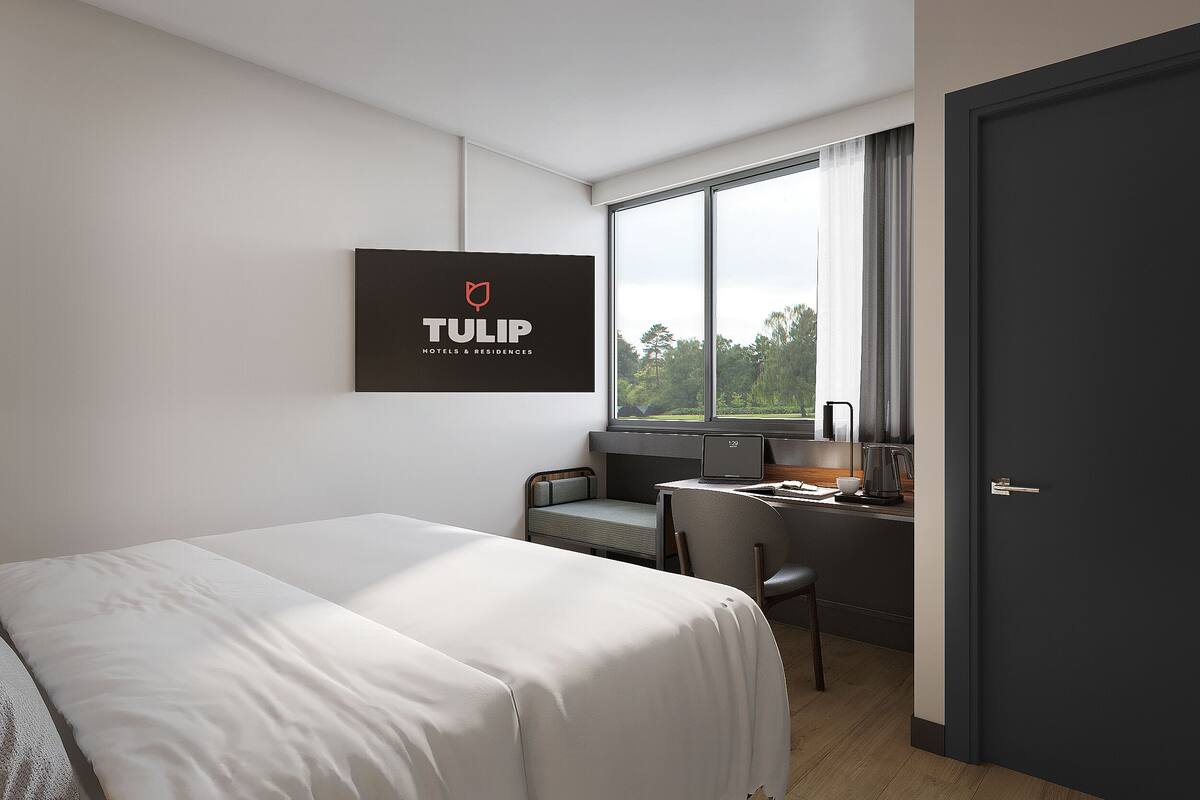 Une chambre d’hôtel moderne équipée d’un lit, d’un bureau, d’une chaise et d’une grande fenêtre.