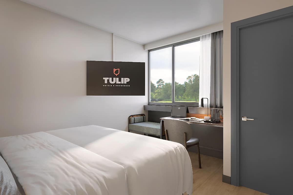 Une chambre d’hôtel moderne équipée d’un lit, d’un bureau, d’une chaise, d’une fenêtre donnant sur un paysage agréable et d’une porte.