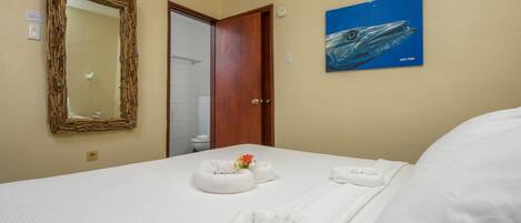 Une chambre d’hôtel avec un lit, un miroir à cadre en bois, un tableau représentant une baleine et une salle de bain visible à travers une porte ouverte.