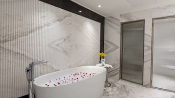A modern bathroom with a freestanding bathtub, a shower enclosure, and marble walls.