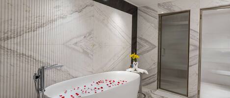 A modern bathroom with a freestanding bathtub, a shower enclosure, and marble walls.