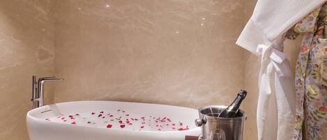Une salle de bain avec une baignoire remplie de pétales de rose, une bouteille de champagne et deux verres posés sur une petite table en bois.
