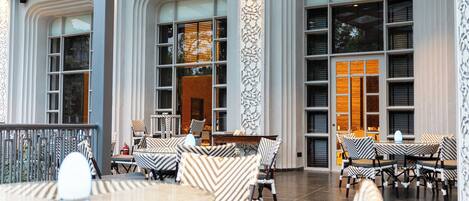 A spacious indoor area with multiple tables and chairs, large windows, and decorative wall panels.