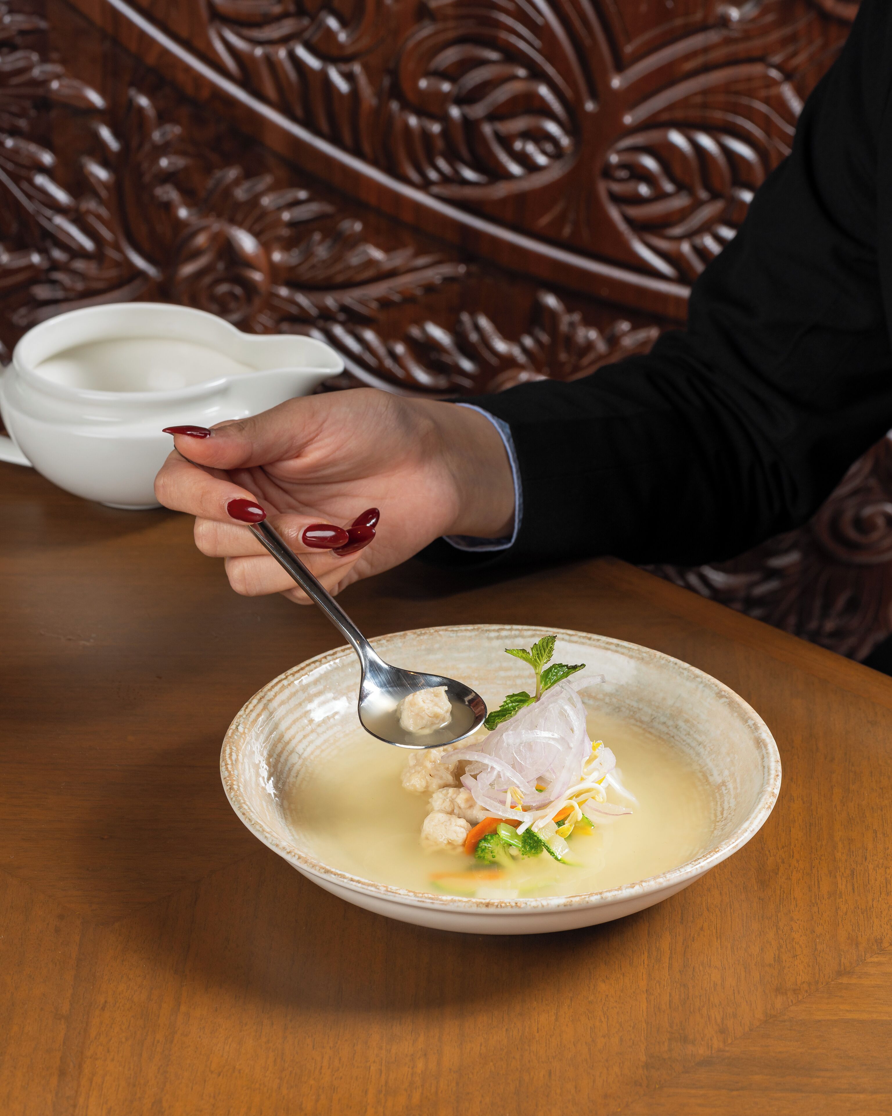 A bowl of soup with a spoon, garnished with herbs, on a wooden table.