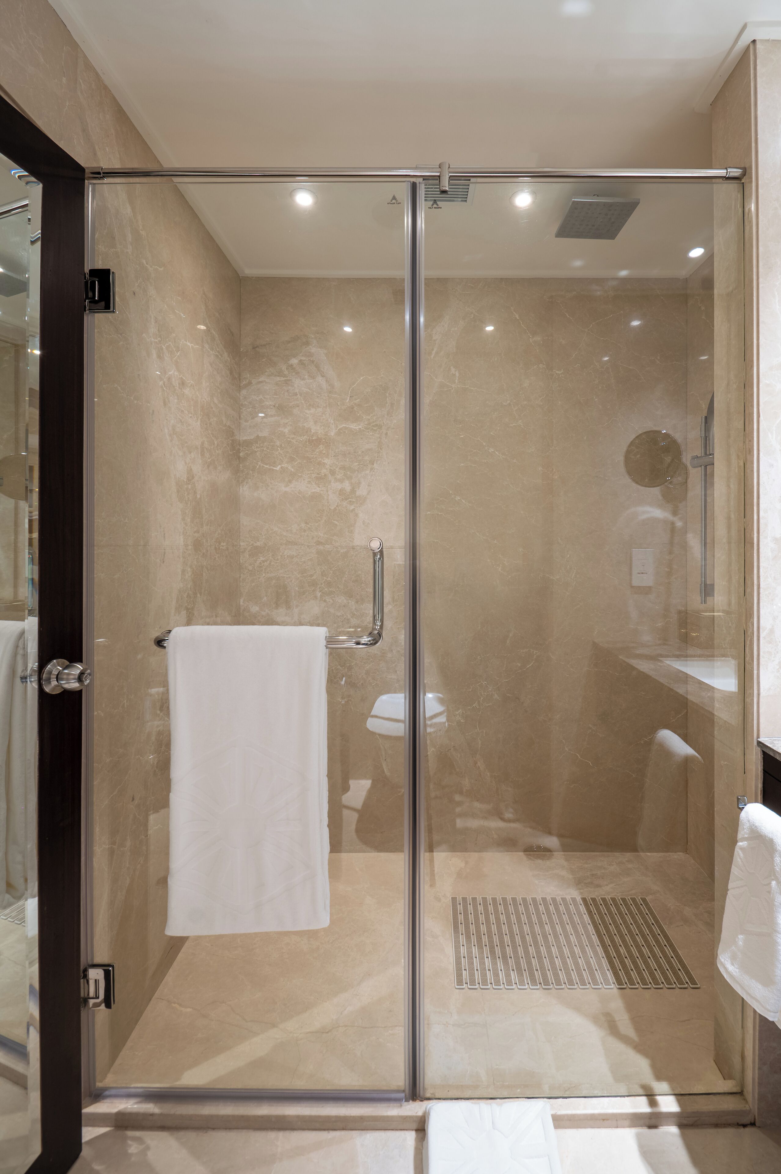A glass-enclosed shower with a white towel hanging on a rack, a glass door, and a showerhead.