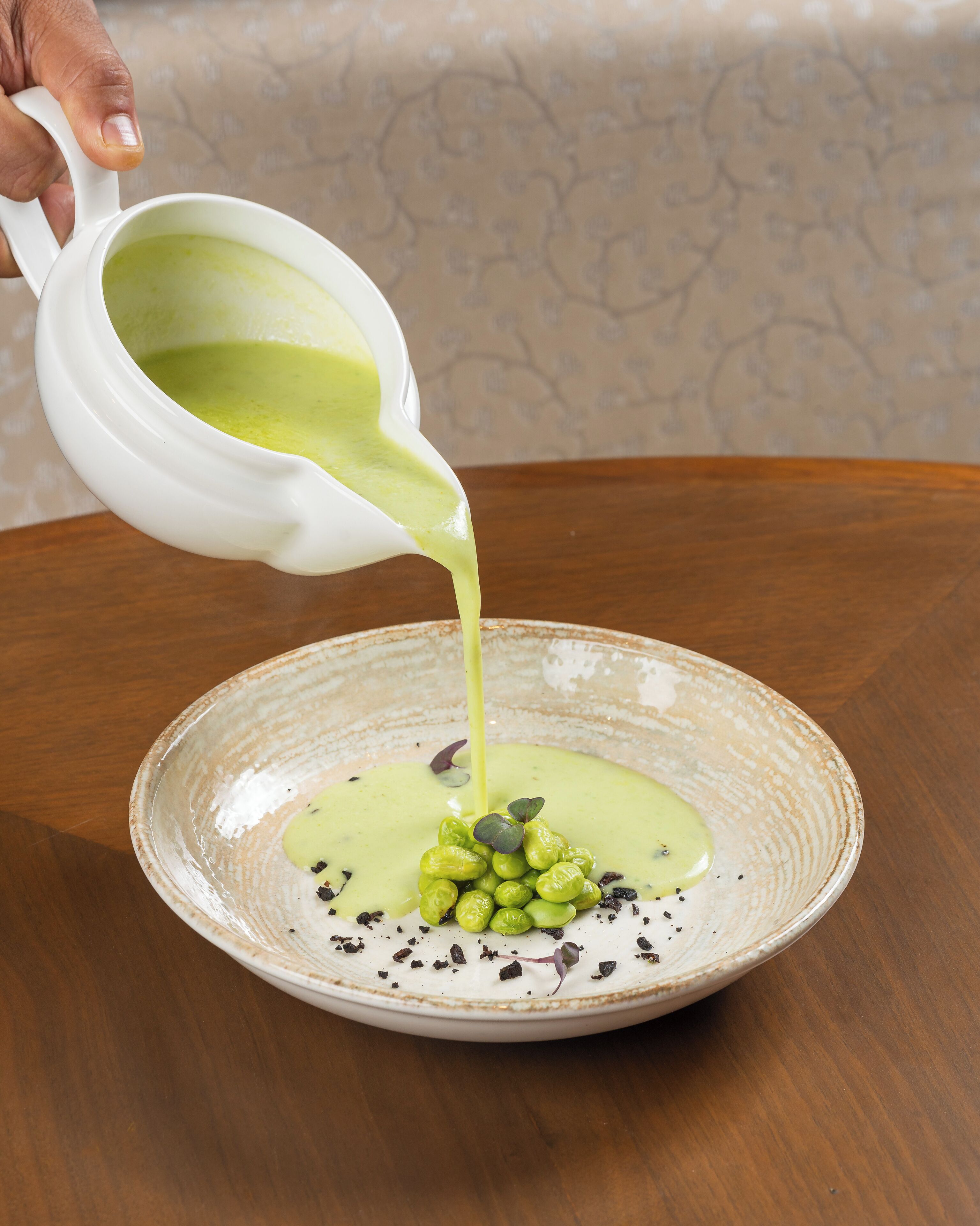 Uma mão despejando um molho verde sobre um prato com vegetais e sementes.
