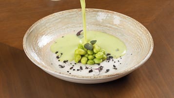 Une main verse une sauce verte sur un plat contenant des légumes verts et des graines.