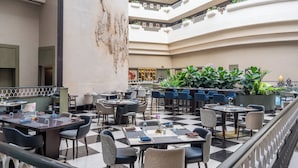A spacious indoor dining area with multiple tables and chairs, a checkered floor, and a balcony with plants. - Taj Deccan (Hyderabad)