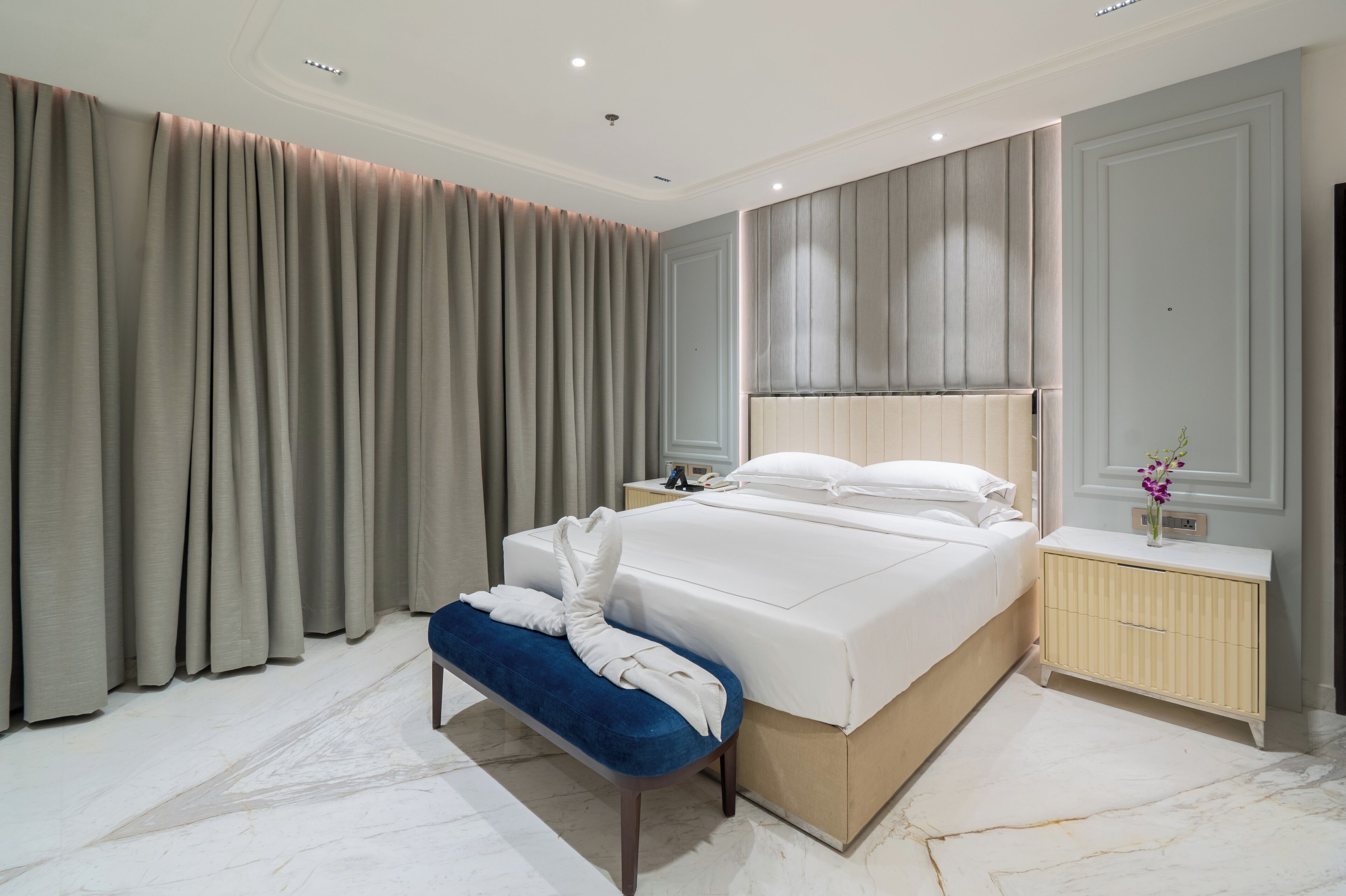 A modern hotel room with a large bed, a bedside table, a bench, and a nightstand.