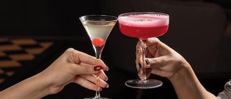 Two hands holding martini glasses with different colored drinks.