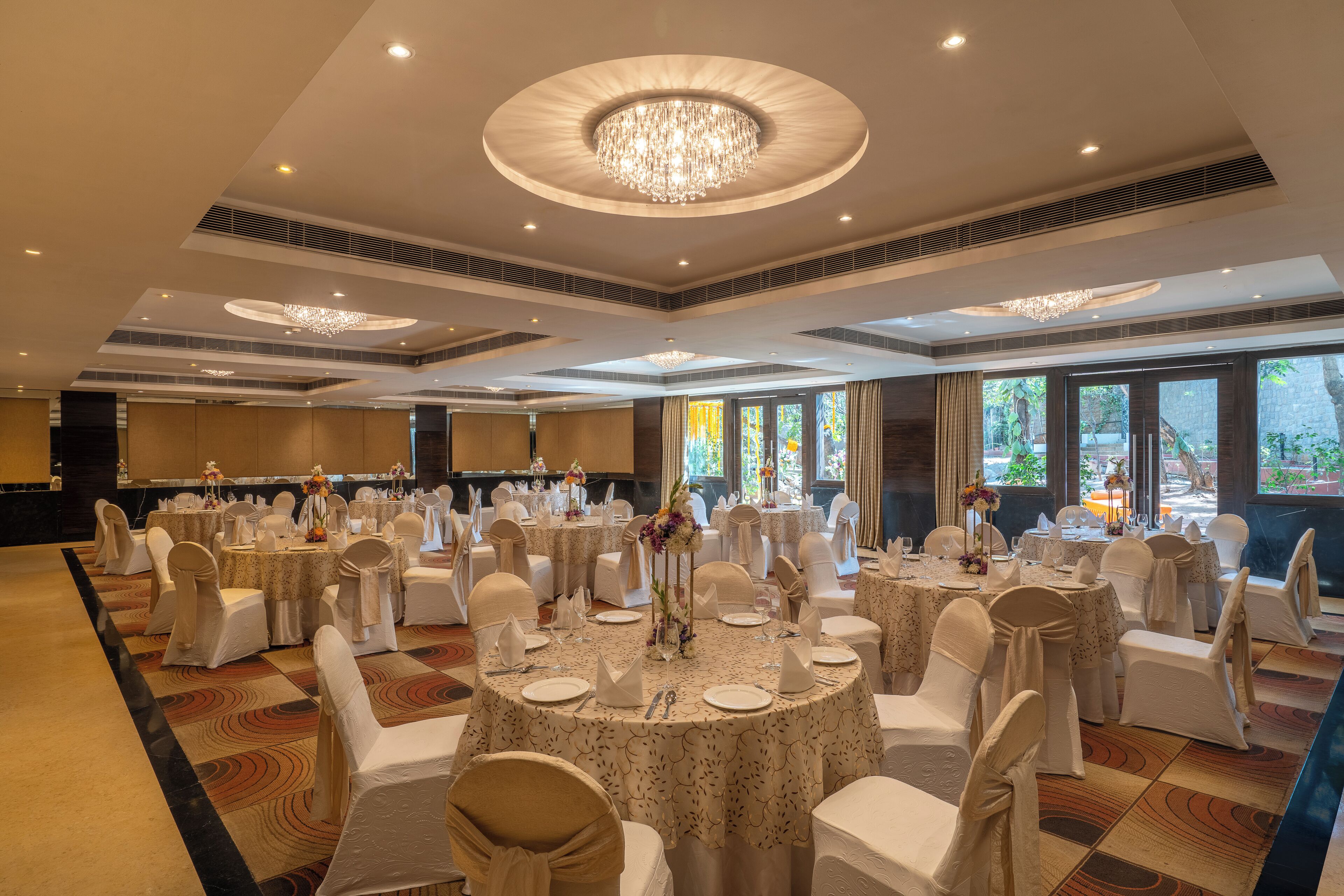 A banquet hall with round tables, white chairs, and chandeliers.