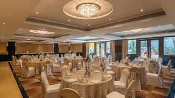 Un salón de banquetes con mesas redondas, sillas blancas y candelabros.